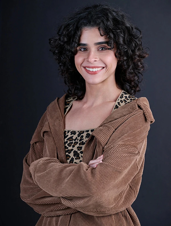 Smiling commercial acting headshot of a woman in a brown jacket with her arms folded.