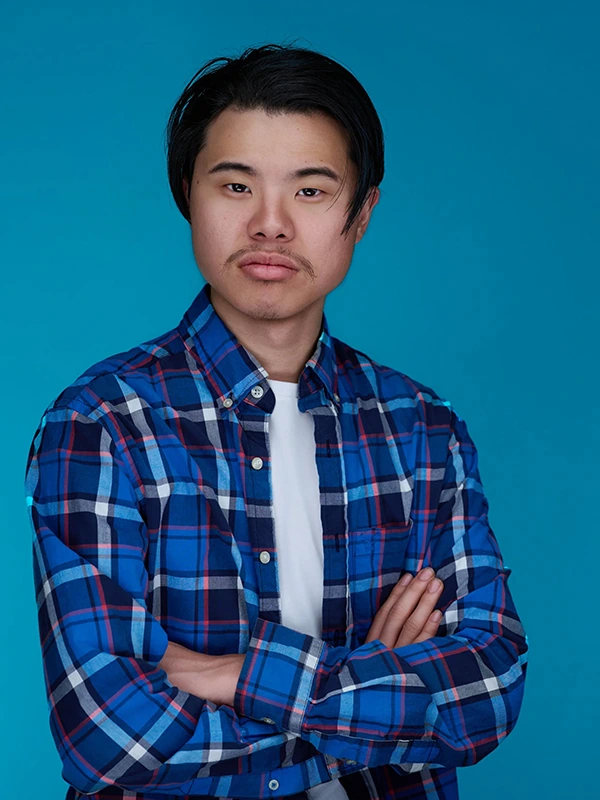 Commercial actor headshot of a young man in a blue plaid shirt against a bright blue background.