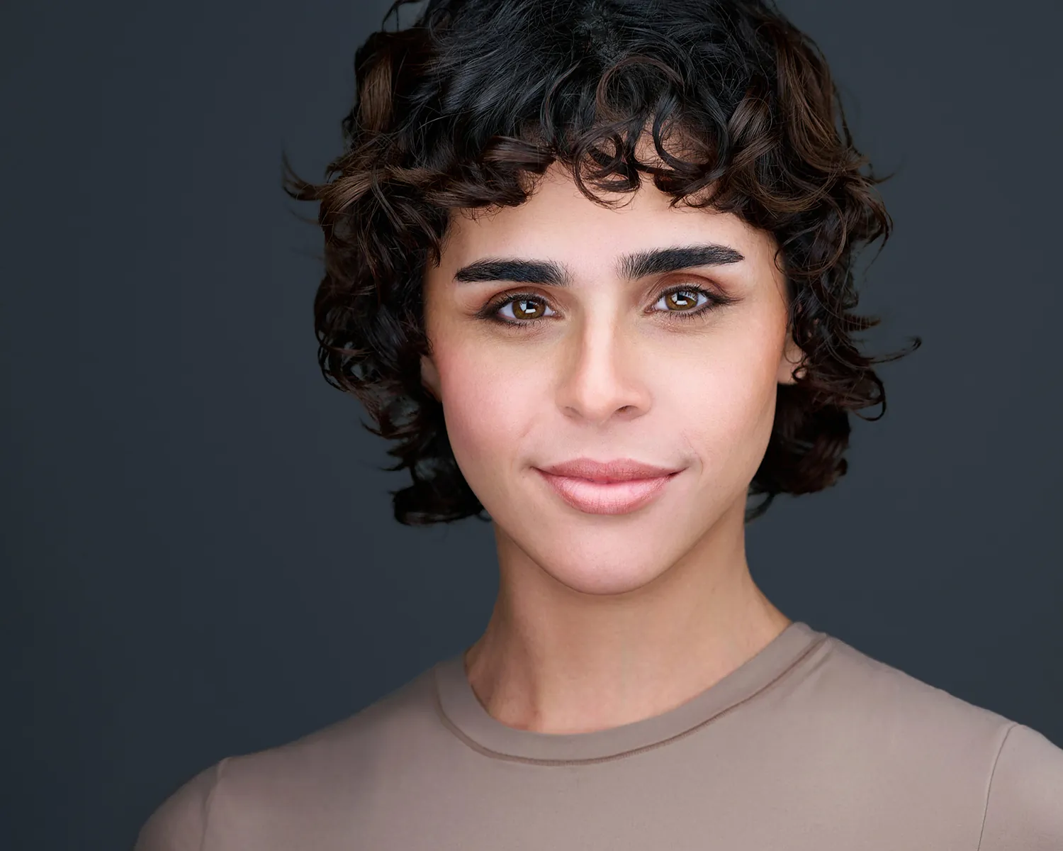 Creative professional headshot of a woman with short curly hair against a gray background.