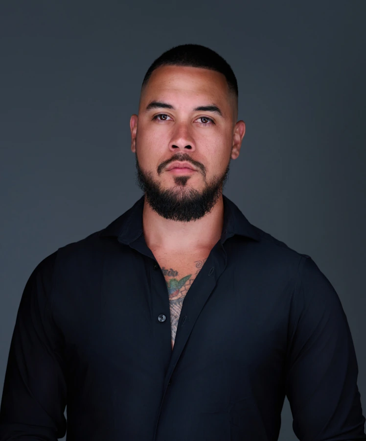 Male actor headshot in black wardrobe with a serious expression against a dark studio background.