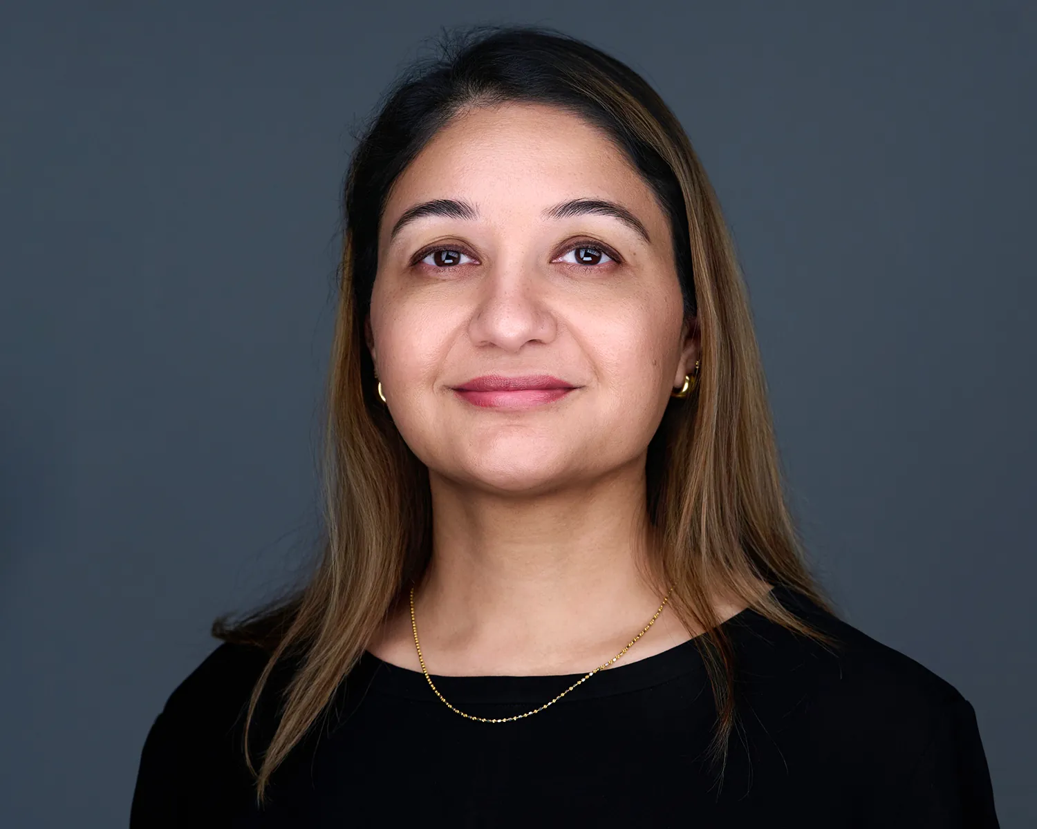Professional headshot of a woman in a black top against a gray studio background.