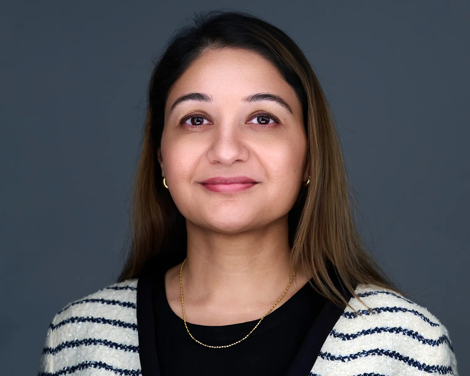 Professional headshot of a woman wearing a striped cardigan against a gray background.