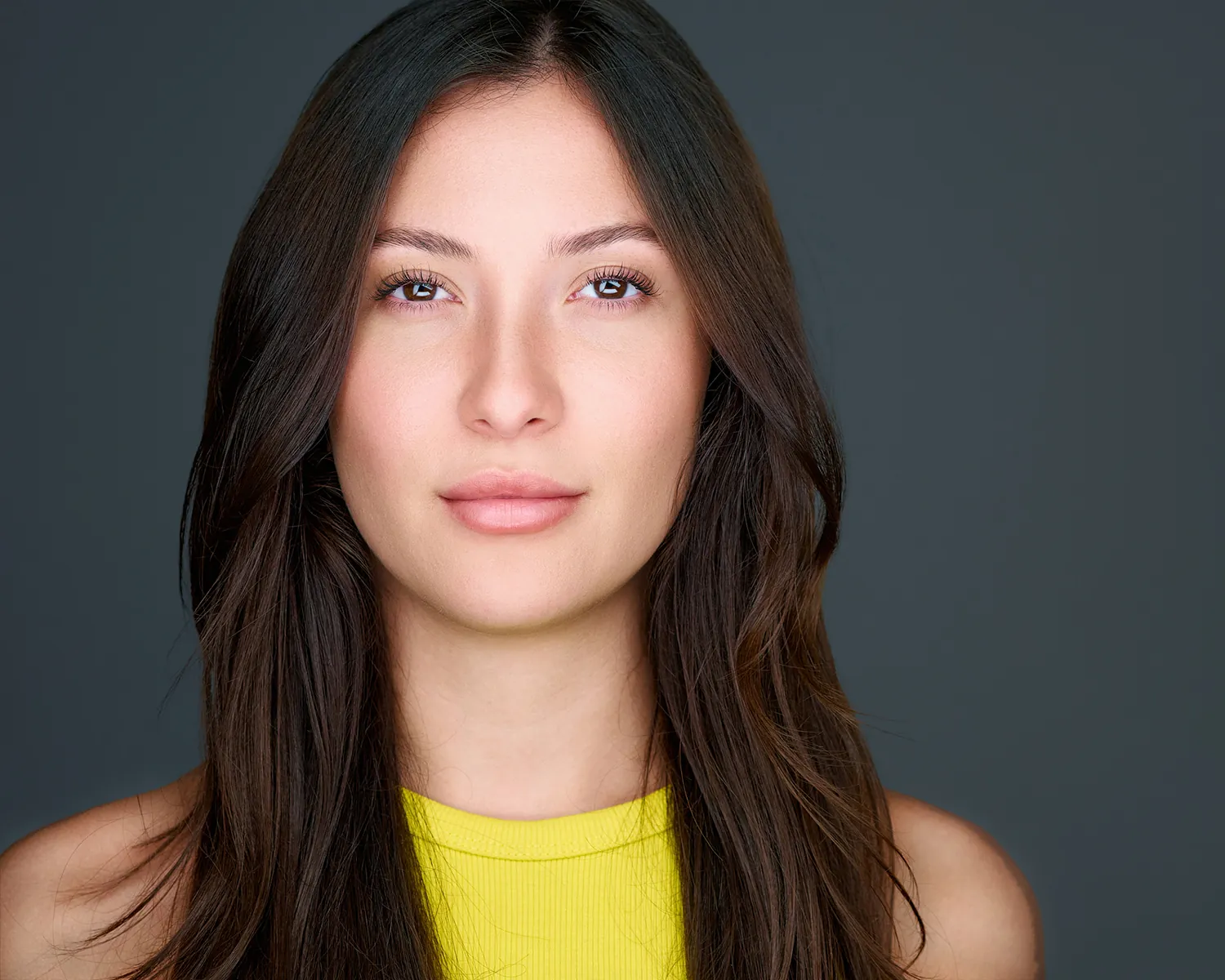 Professional headshot of a woman in a yellow top against a gray studio background.